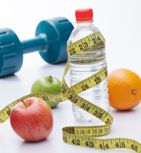 An assortment of apples and dumbbells arranged next to a bottle of water on a white background.